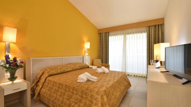 Camera con letto, TV e balcone con tende.