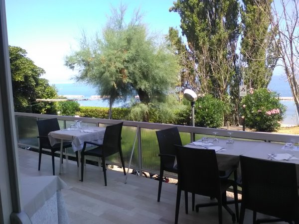 Tavoli all'aperto con vista mare e alberi.