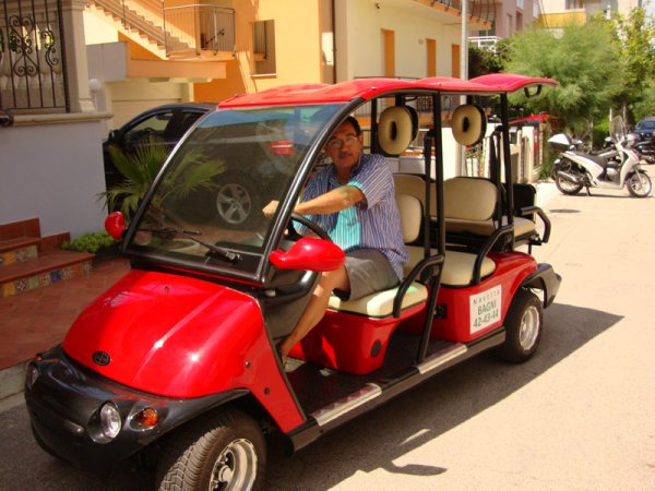 Persona alla guida di un carrello da golf rosso in una strada.