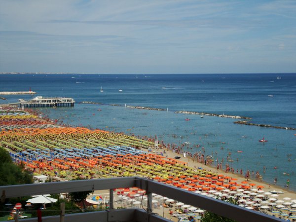 Spiaggia affollata con ombrelloni colorati e mare azzurro.