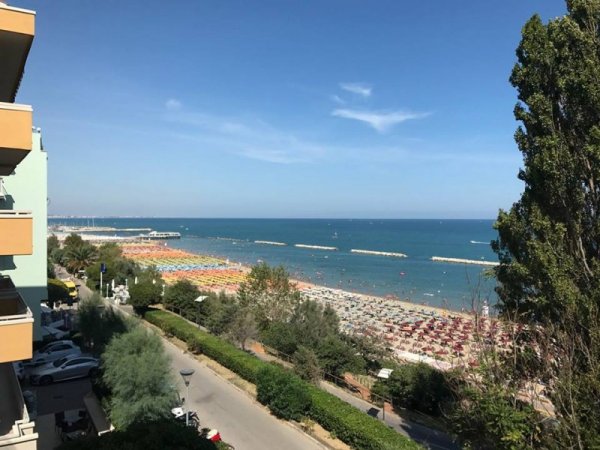 Spiaggia vista dall'alto con mare e ombrelloni.