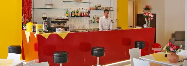 Bancone rosso con bartender e sgabelli neri.