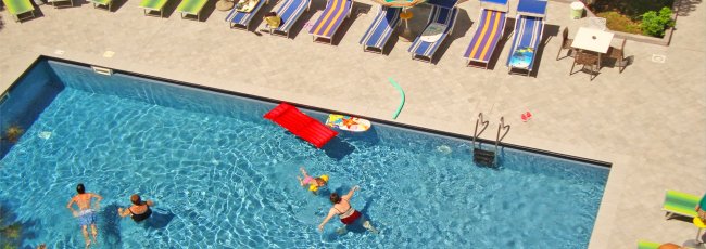 Piscina con persone che nuotano e lettini a bordo.