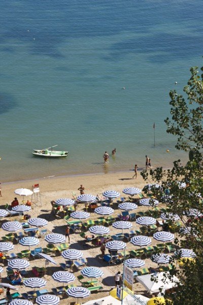 Spiaggia vista dall'alto con ombrelloni a righe e una barca.