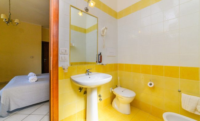 Bagno con piastrelle gialle e bianche, lavandino e WC.