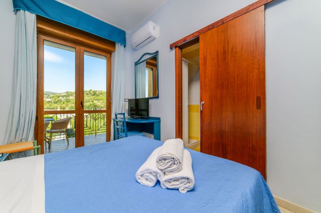 Letto matrimoniale con balcone e vista collinare.