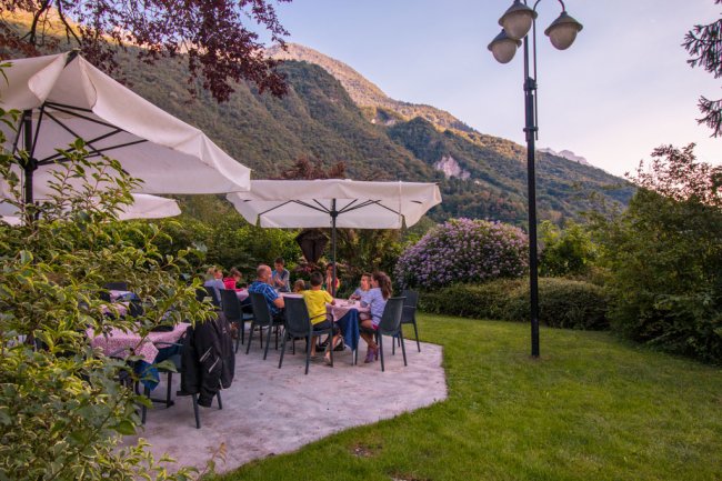 Persone sedute a tavolino sotto ombrelloni bianchi in giardino.