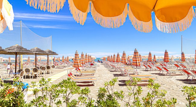Spiaggia con ombrelloni e lettini allineati.