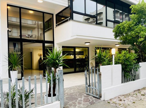 Ingresso hotel moderno con piante e cancello aperto.
