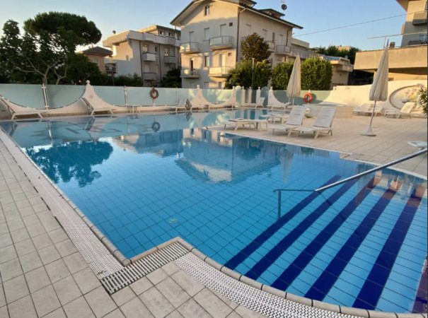 Piscina con lettini e ombrelloni in un ambiente residenziale.