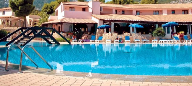 Piscina con ponticello e ombrelloni blu, albergo sullo sfondo.