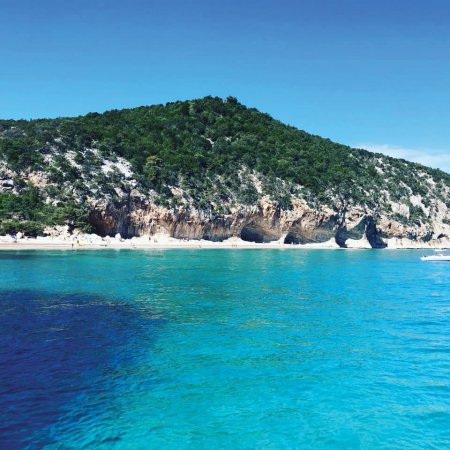 Spiaggia con mare turchese e colline verdi.