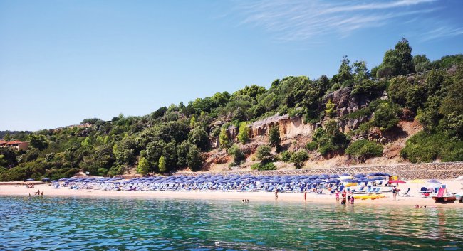 Spiaggia con ombrelloni blu e verde collina.