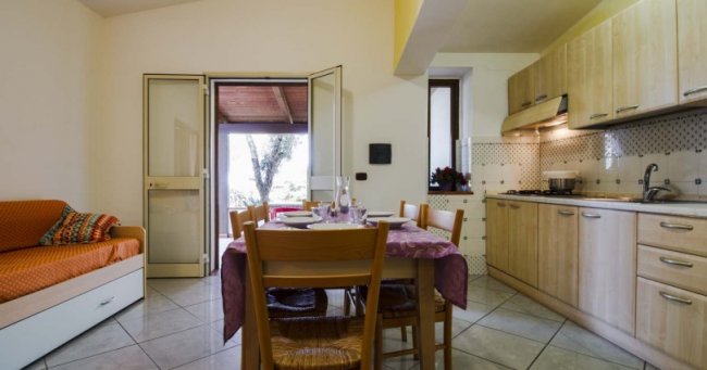 Cucina e sala da pranzo con tavolo apparecchiato, divano arancione e accesso all'esterno.