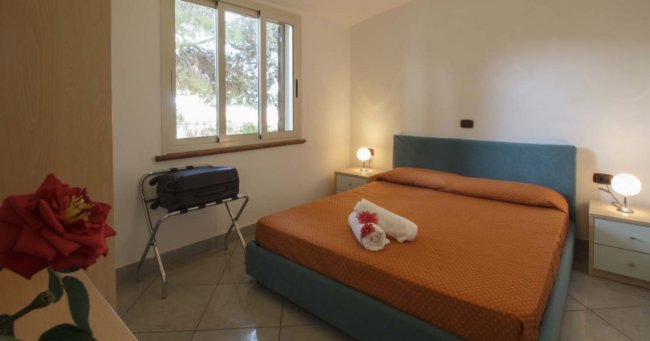 Camera da letto con letto matrimoniale arancione, due comodini con lampade accese e una finestra.