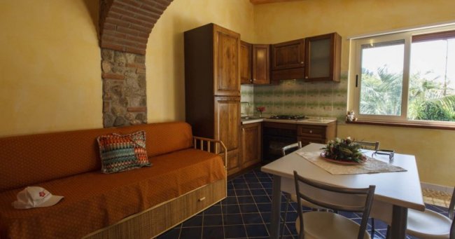 Cucina con divano arancione, tavolo bianco e arredi in legno. Finestra sulla destra.