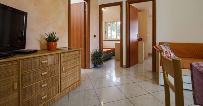 Interno di una casa con mobili in rattan, pavimento piastrellato e piante.