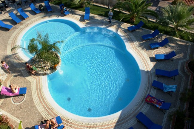 Piscina a forma di trifoglio con lettini blu intorno.