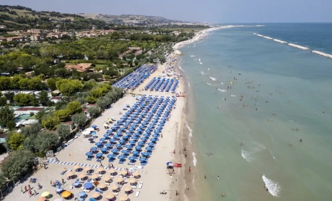 Spiaggia con ombrelloni blu e gente in mare.