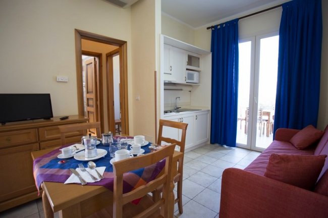 Soggiorno con divano rosso, tavolo blu e accesso a balcone.