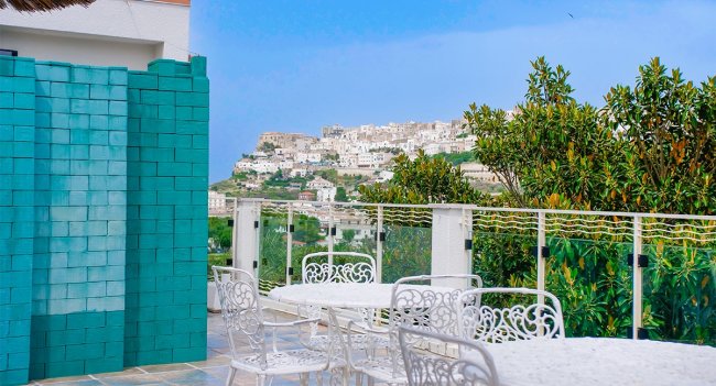 Terrazza con tavolini bianchi e vista su un paesaggio collinare.