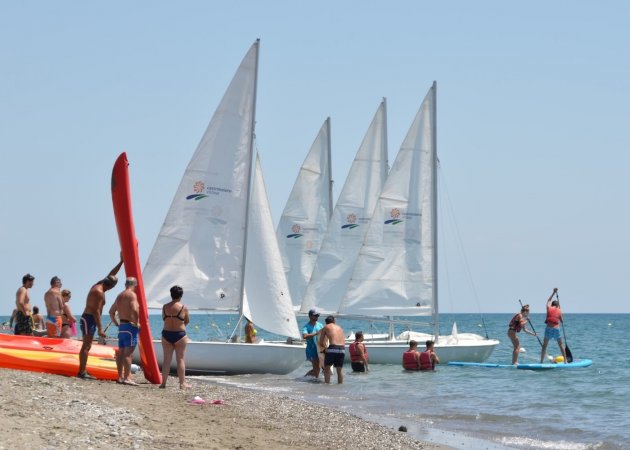 Persone sulla spiaggia, barche a vela in acqua.