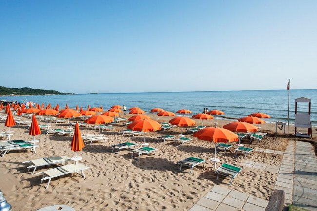 Spiaggia con ombrelloni arancioni e lettini verdi.