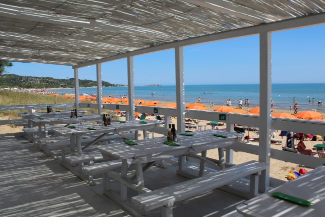 Tavoli all'aperto su una terrazza vista mare con ombrelloni arancioni.