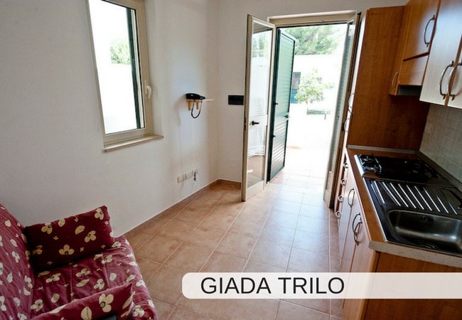 Soggiorno con angolo cottura e porta aperta verso l'esterno.