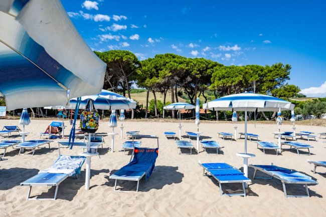 Spiaggia sabbiosa con ombrelloni bianchi e blu.
