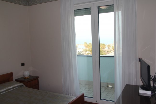 Stanza con letto, porta finestra e vista mare.