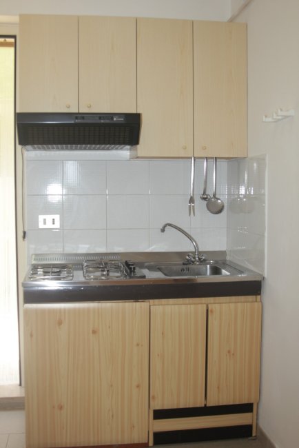 Cucina compatta, legno chiaro, fornelli e lavello.