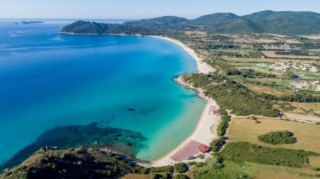 Una baia con mare turchese e spiaggia sabbiosa vista dall'alto, circondata da colline verdi.
