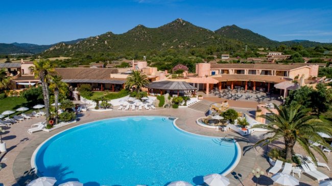 Piscina grande con sedie a sdraio, palme e vista su colline verdi.