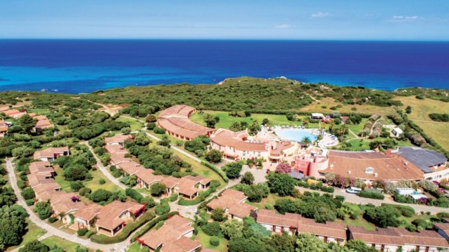 Vista aerea di un resort costiero circondato da cespugli verdi e con il mare all'orizzonte.